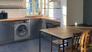 A compact kitchen with a washing machine, a sink, and a wooden dining table with chairs. - Southfield Art Studio (Braunston, near Daventry)