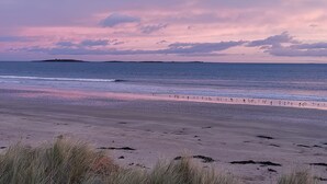 Une plage avec un large rivage sablonneux, une mer calme et une île qui se dessine à l’horizon.