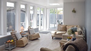 Un salon spacieux avec de grandes fenêtres, un canapé, un fauteuil et une table avec une lampe.