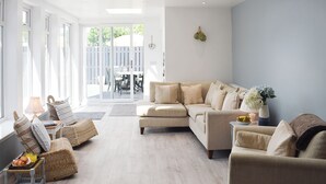 Un salon spacieux avec un canapé beige, une petite table d’appoint et un fauteuil en osier.