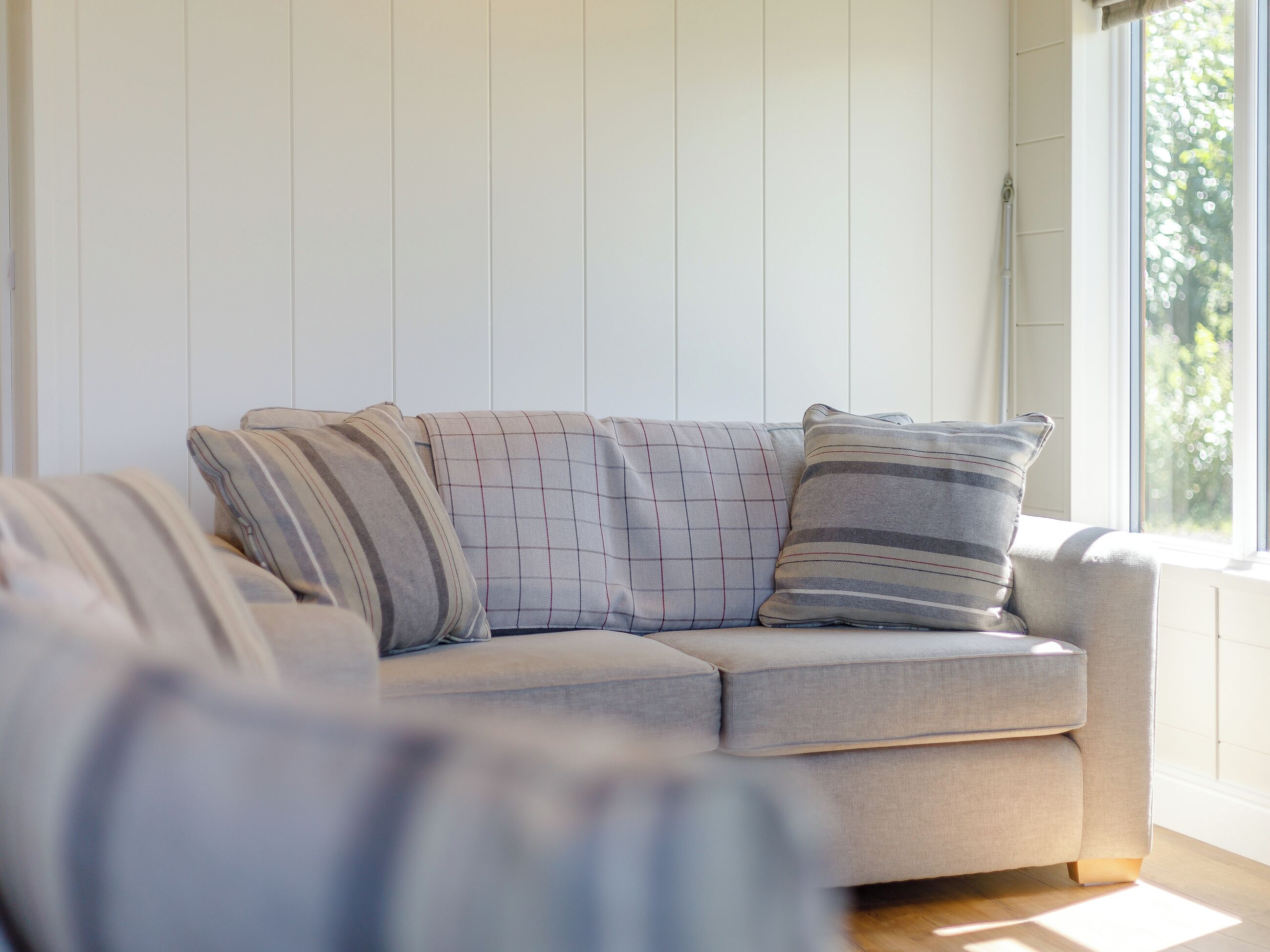 A light-colored sofa with striped pillows in a room with white paneled walls and a window.