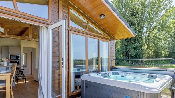 Un área moderna de hidromasaje al aire libre con una terraza de madera, una puerta de vidrio que da a una cocina y vistas de la vegetación circundante.