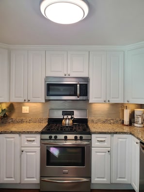 Una cocina con gabinetes blancos, estufa de acero inoxidable, microondas y cocina a gas.