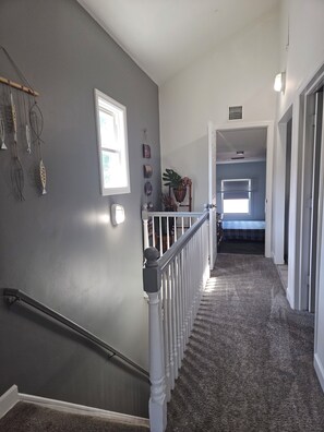 Un couloir doté d’un sol recouvert de moquette, d’une rambarde blanche et d’un escalier menant à une autre pièce.
