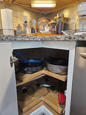 A kitchen with a countertop, a coffee machine, and a storage cabinet with pots and pans.