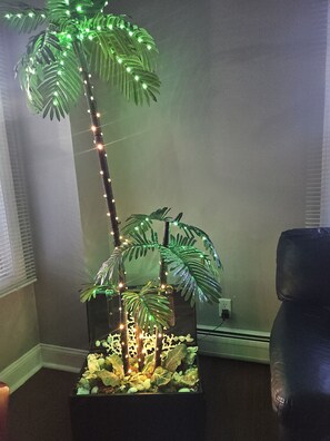 A room with a corner plant display featuring artificial palm trees and a decorative base.