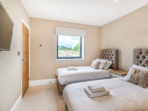 A bedroom with two beds, a window with a view, a TV mounted on the wall, and a wooden door. - UK34190 - Gowan View (Arkholme, near Kirkby Lonsdale)