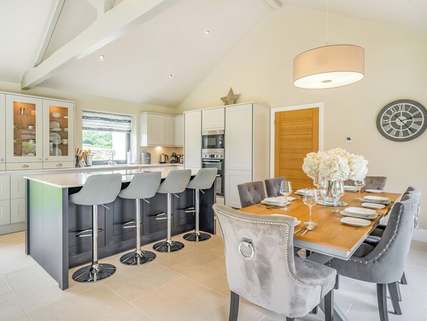 A modern kitchen with a central island, bar stools, and a dining area with a wooden table and chairs.