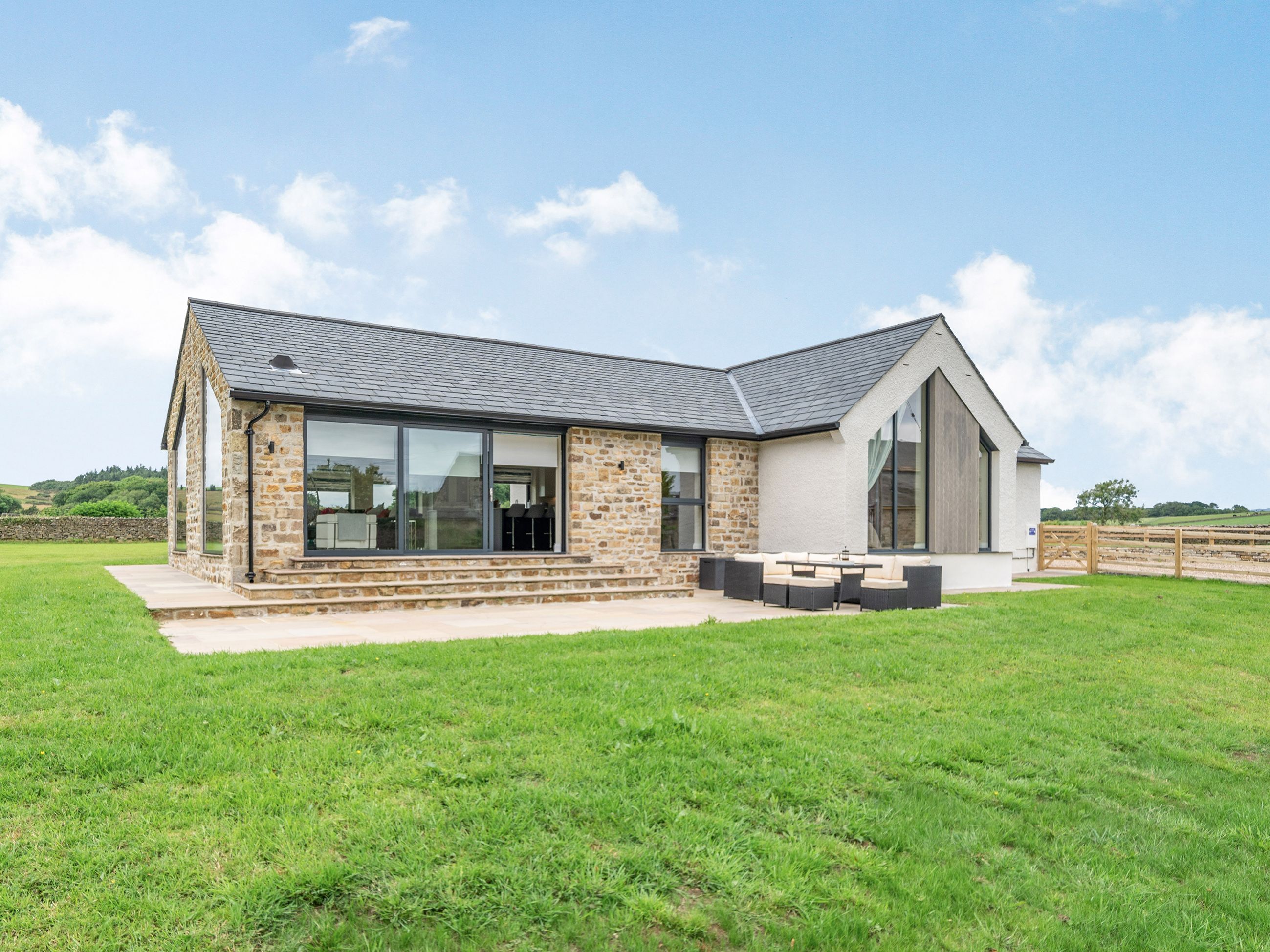 A modern house with a stone exterior, large windows, and a patio area.