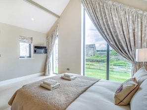 A bedroom with a large bed, a TV mounted on the wall, and a window with curtains.