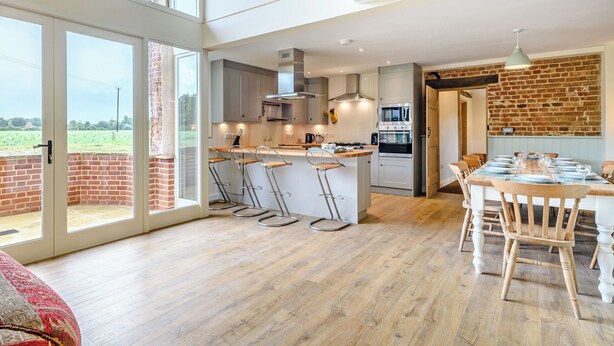A modern kitchen with a large island, bar stools, and a dining area with a brick wall.