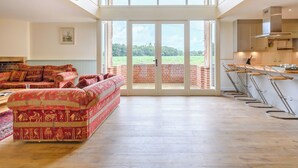 A spacious living area with a large window, a patterned sofa, and a kitchen with bar stools.