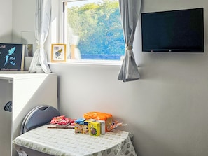 Ein Zimmer mit Fenster, einem Flachbildfernseher, einem Tisch mit Kinderspielzeug und einem Stuhl.