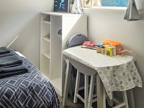 Ein Schlafzimmer mit Bett, Schreibtisch und Stuhl. Auf dem Schreibtisch liegen Bücher und eine Schachtel.