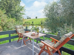 Une terrasse avec une table et deux chaises, donnant sur un étang et une végétation luxuriante.
