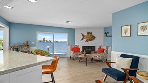 Un salon spacieux doté d’une grande fenêtre donnant sur un plan d’eau, d’une cheminée et de différents types de sièges.