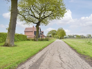 A rural road leading to a brick house with a large tree on the left. - 1 bedroom accommodation in Bures (Bures)