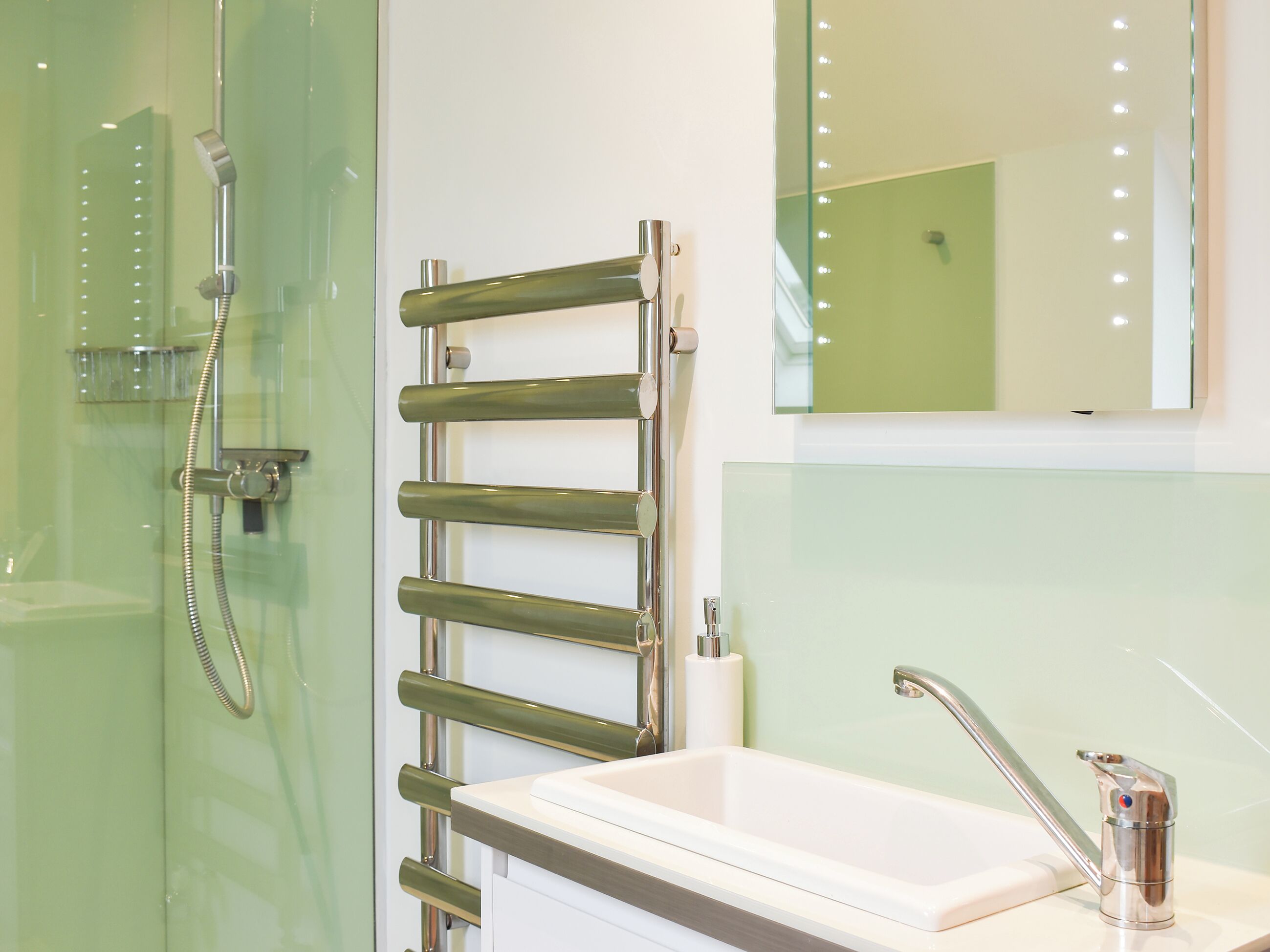 A bathroom with a glass shower enclosure, a towel rack, a sink with a chrome faucet, and a mirror with lights.