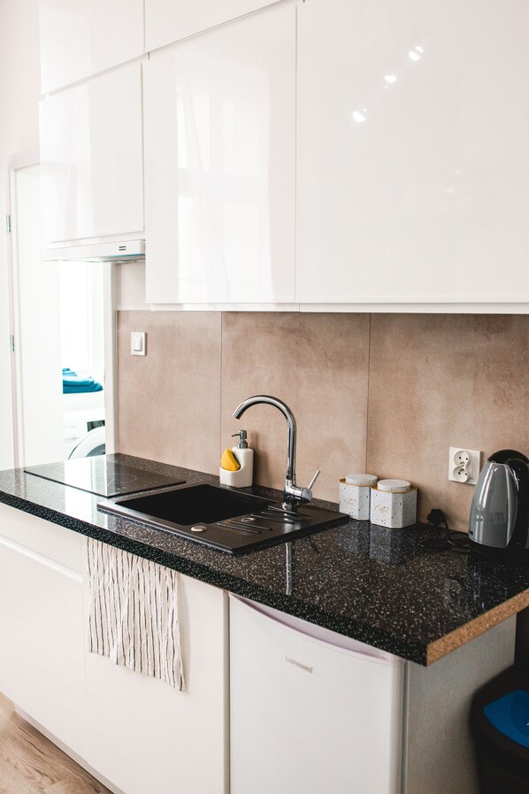 A modern kitchen with white cabinets, a black countertop, a stainless steel sink, and a kettle.