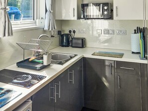 A modern kitchen with a built-in microwave, toaster, and kettle. There is a sink with a drying rack, and a window with curtains.