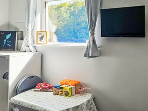A room with a window, a flat-screen TV, a table with children's toys, and a chair.