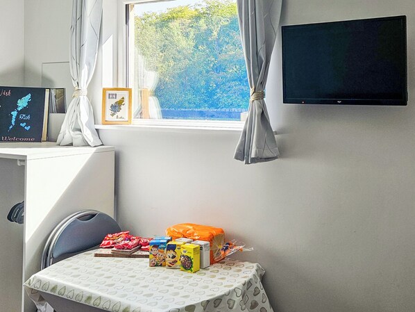 A room with a window, a flat-screen TV, a table with children's toys, and a chair.