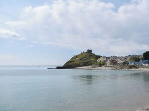 A coastal town with a prominent hill featuring a castle-like structure, a sandy beach, and a calm sea.