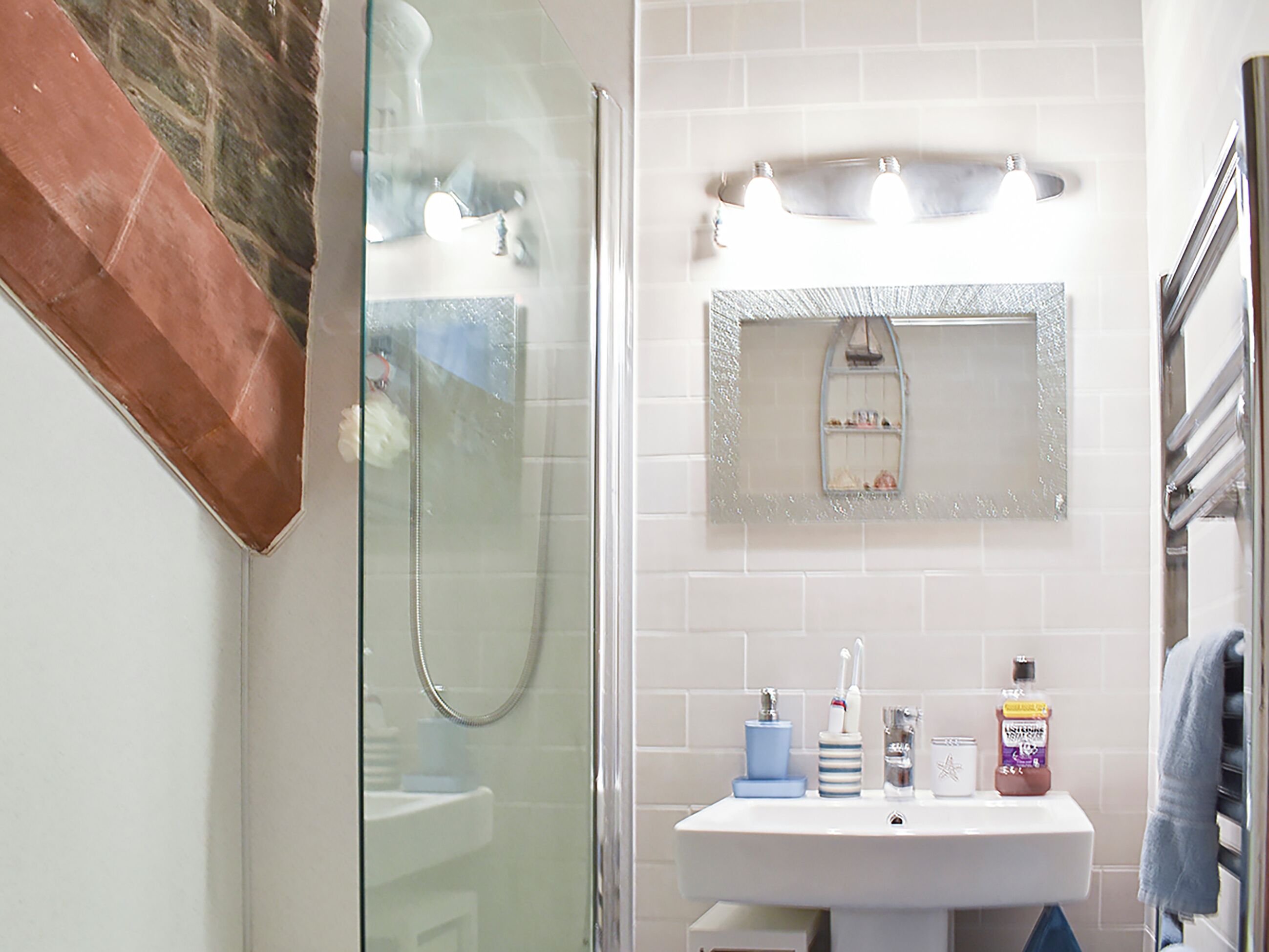 Un bagno con cabina doccia in vetro, lavandino bianco con articoli da toilette e specchio sopra il lavandino.