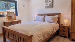 A bedroom with a wooden bed, bedside tables, a nightstand, a mirror, and a window with a view of trees. - 5 bedroom accommodation in Somerton (Somerton)