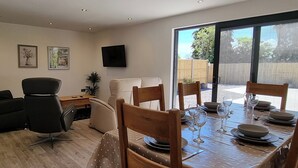 A dining area with a table set for four, a sofa, a TV on the wall, and a view of the outdoors. - 5 bedroom accommodation in Somerton (Somerton)