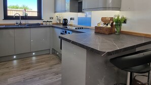 A modern kitchen with grey cabinets, a black countertop, a window with a view, and a bar stool. - 5 bedroom accommodation in Somerton (Somerton)