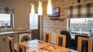 Een keuken met een wasmachine, een eettafel met stoelen, een aan de muur bevestigde televisie en een raam met uitzicht.