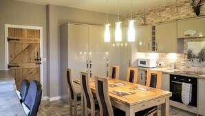Een eetgedeelte met een houten tafel en stoelen, een keuken met een magnetron, en een stenen muur.