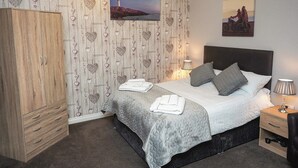 Een slaapkamer met een bed, nachtkastjes, een kledingkast, een schilderij van een vuurtoren, en een wand met decoraties in de vorm van harten.