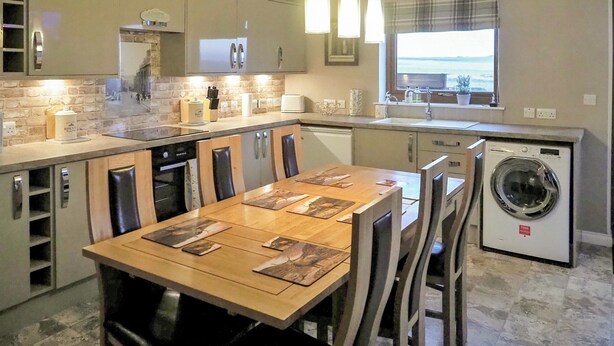 Een moderne keuken met een bakstenen muur, een eethoek met een houten tafel en stoelen, en een ingebouwde wasmachine.