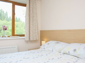 Ein Schlafzimmer mit Bett, Fenster mit Vorhängen, Heizkörper und Nachttisch mit Lampe.