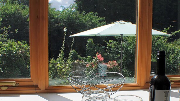 A window with a view of a garden, a bottle of wine, and two glasses on a table. - 2 bedroom accommodation in Snodland (Snodland)