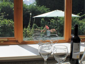 Une fenêtre donnant sur un jardin, une bouteille de vin et deux verres sur une table.