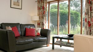 A living room with a leather sofa, a table with magazines, a lamp, and a large window with curtains. - 2 bedroom accommodation in Snodland (Snodland)