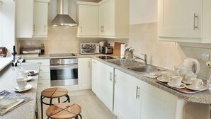 A compact kitchen with white cabinets, stainless steel appliances, and a small dining area with stools. - 2 bedroom accommodation in Snodland (Snodland)