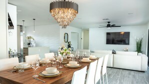 A modern dining room with a wooden table set for a meal, white chairs, and a chandelier. - Scottsdale Luxury Escape (Scottsdale)