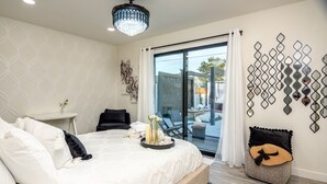 A modern bedroom with a large bed, a small table, a chair, and a decorative wall piece. - Scottsdale Luxury Escape (Scottsdale)