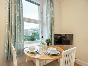 A dining area with a round wooden table, white chairs, and a TV on the wall. - 1 bedroom accommodation in Largs (Largs)