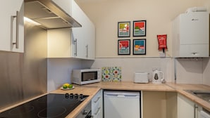 A modern kitchen with a built-in stove, microwave, toaster, and dishwasher. There are framed pictures on the wall and a fire blanket on the wall.