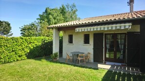 A small house with a tiled roof, a patio with a table and chairs, and a well-maintained garden. - Maison Individuelle Dans le Calme et la Verdure (Labarthe-sur-Lèze)