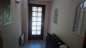 A narrow hallway with a door featuring a grid of square windows, a radiator, a small table with items, and a wall-mounted window. - Maison Individuelle Dans le Calme et la Verdure (Labarthe-sur-Lèze)