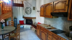 A kitchen with wooden cabinets, a tiled backsplash, a clock, and a fireplace. - Maison Individuelle Dans le Calme et la Verdure (Labarthe-sur-Lèze)