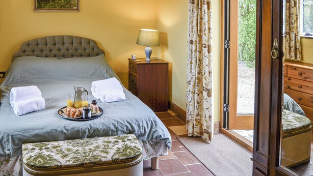 Ein Schlafzimmer mit Bett, Nachttisch, Lampe und Blick ins Freie.
