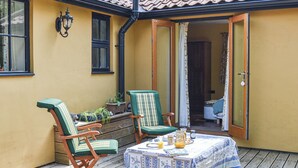 Eine Terrasse im Freien mit zwei Holzstühlen, einem Tisch mit blau-weißer Tischdecke und einem Blumentopf.