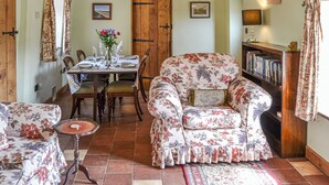 Ein Essbereich mit einem Holztisch, gedeckt für vier Personen, einem floralen Sessel und einem Bücherregal mit Büchern.
